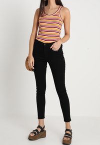 Randig linne med rosa, orange och gula ränder, kombinerat med högmidjade svarta jeans och träplattformssandaler. Tillbehören inkluderar en rund väska.