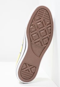 Żółta podeszwa trampka z płótna z brązowym wzorem z gumy, białą krawędzią z gumy oraz logo marki "Converse All Star". Posiada teksturowany wzór antypoślizgowy.