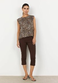 Top bez rukávů s leopardím potiskem v kombinaci s hnědými zkrácenými kalhotami. Modelka stojí v sandálech na podpatku, předvádí hladkou texturu a ležérní střih.