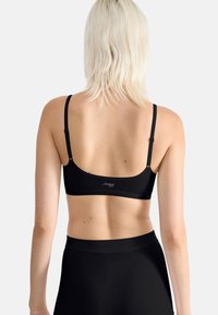 Black sports bra with adjustable straps, smooth texture, and logo on the back. Paired with high-waisted black leggings.