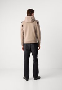 Sweatshirt à capuche beige clair, avec des accents sombres sur les côtés. Assorti à un jean en denim noir, les deux ayant une coupe décontractée. Texture lisse.