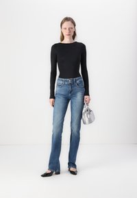 Black long-sleeve top with embellishments, blue straight-leg jeans, black patent loafers, and a small silver handbag.