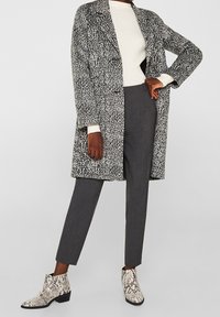 Manteau long à motifs noir et blanc, pull blanc ajusté, pantalon gris sur mesure, et bottines à motifs serpent.