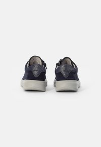 Marineblaue Wildledersneaker mit einer strukturierten Rückseite, hellgrauen Gummisohlen und Reißverschlüssen an den Seiten. Einfaches und unauffälliges Design.