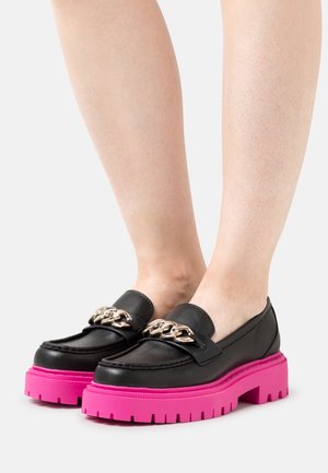 Mocassins en cuir noir avec une épaisse semelle plateforme rose et un détail de chaîne métallique sur le cou-de-pied. Texture lisse et design à bout arrondi.