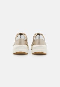 Beige tenisky s texturovaným svrškem, stříbrnými akcenty na patě a silnou bílou podrážkou s gumovým dnem. Kulatý tvar špičky.