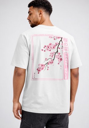 Mann, der von hinten zu sehen ist, trägt ein weißes T-Shirt mit einem pinken Kirschblütenzweig und japanischem Text auf dem Rücken.