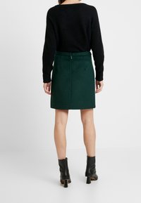 Donkergroene wollenblend rok met een recht model, achterste ritssluiting en een zoomlengte boven de knie, gecombineerd met zwarte enkellaarsjes.