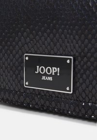 Sac à main synthétique noir texturé avec un motif en écailles, doté d'une plaque logo rectangulaire en argent marquée "JOOP! JEANS."