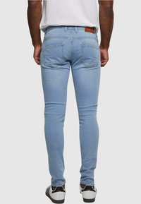 Világoskék, skinny farmernadrág, két hátsó zsebbel és barna bőrcímkével a deréknál. Fehér és fekete sportcipővel viselve.