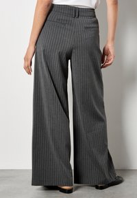 Pantaloni grigi a righe, a gamba larga, con vita alta. Presentano due tasche posteriori e una texture liscia. Includono pieghe sottili.