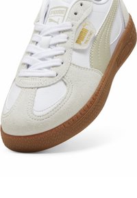 Weiße und hellgraue Sneaker mit einem Obermaterial aus Wildleder und Leder, runder Zehenpartie, weißen Schnürsenkeln und einer strukturierten Gummisohle, die Logoprints aufweist.