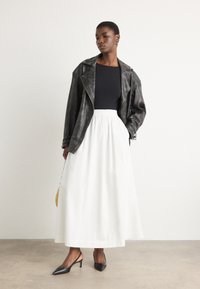 Veste de moto en cuir noir, haut noir ajusté, jupe blanche fluide et escarpins pointus noirs. Comprend un petit sac à main jaune.