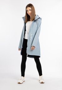 Jasnoniebieski wodoodporny płaszcz z kapturem, z suwakiem z przodu i sznurkiem. W połączeniu z czarnymi legginsami i białymi sneakersami. Minimalistyczny design.