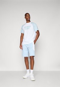 Lys blå og hvit treningsdrakt med raglanermer, med "Los Angeles Dodgers" trykk og matchende shorts i mykt stoff.
