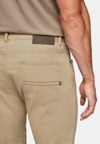 Beige trousers made of cotton with a straight cut. Features a leather label on the waistband and a single back pocket with visible stitching.