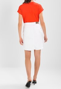 Top rosso a maniche corte abbinato a una gonna in denim bianco con orlo sfrangiato, tasche posteriori e una piccola etichetta con logo sulla vita.