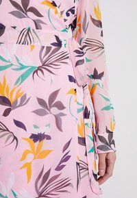 Abito avvolgente rosa con un motivo floreale in viola, giallo e verde. Realizzato in tessuto leggero, con maniche lunghe e dettaglio di vita annodata.
