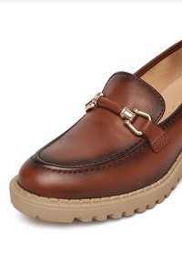Hnědé kožené mokasíny s akcentem zlaté přezky, kulatou špičkou a gumovou podrážkou s texturovaným vzorem pro lepší přilnavost.