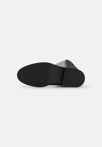 Suela de zapato negra con un acabado suave, que presenta un borde cosido y una suela de agarre con patrón. Diseño ligero con una forma estilizada.