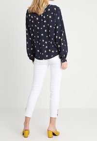 Marinblå blommig blus med lång ärm och små färgglada blommor; kombinerad med vita figursydda byxor med kilklipp och gula blockklacksandaler.