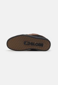 Chaussure de skate marron et noire avec une semelle en caoutchouc texturée, présentant un motif de bande de roulement prononcé ainsi que le logo "GLOBE".