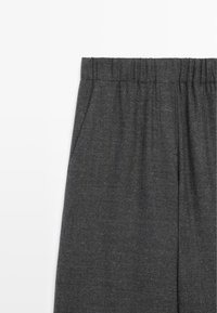 Zbliżenie na ciemnoszare spodnie z elastycznym pasem i widoczną boczną kieszenią na białym tle.