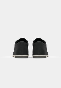 Zapatillas negras con textura suave y forma redondeada. Presentan una suela de color claro y un diseño minimalista. La vista trasera muestra un tacón plano.