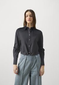 Σκούρο μπλε πουκάμισο με γιακά, μακριά μανίκια και κομψό σχεδιασμό. Διαθέτει έναν διακριτικό λογότυπο και λεπτομέρεια στη σφιχτή μέση.