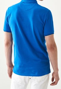 Modrá polokošile vyrobená z bavlny s krátkým rukávem a žebrovaným límečkem. Obsahuje kontrastní lemování na rukávech a lemu.