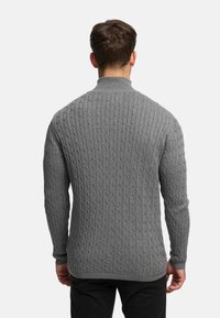 Grå kabelstickad tröja med hög krage, med texturerade ribbade mönster och långa ärmar. Diskreta detaljer vid muddar och fåll.