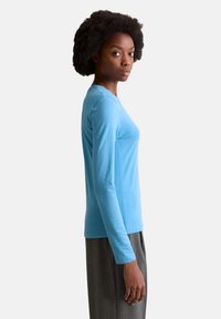 Light blue long-sleeve shirt, soft cotton fabric, fitted design, round neckline, paired with gray pleated trousers. No visible patterns or accents.