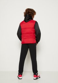 Czerwona pikowana kamizelka z czarnymi rękawami, z kapturem. Noszona z czarnymi spodniami i czerwonymi trampkami. Gładka tekstura, casualowy design.