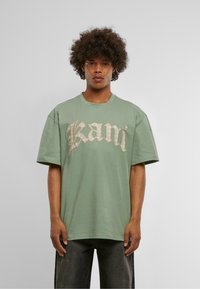 Light green cotton t-shirt with short sleeves. Features large scripted text "Kani" in a metallic gold accent across the chest.