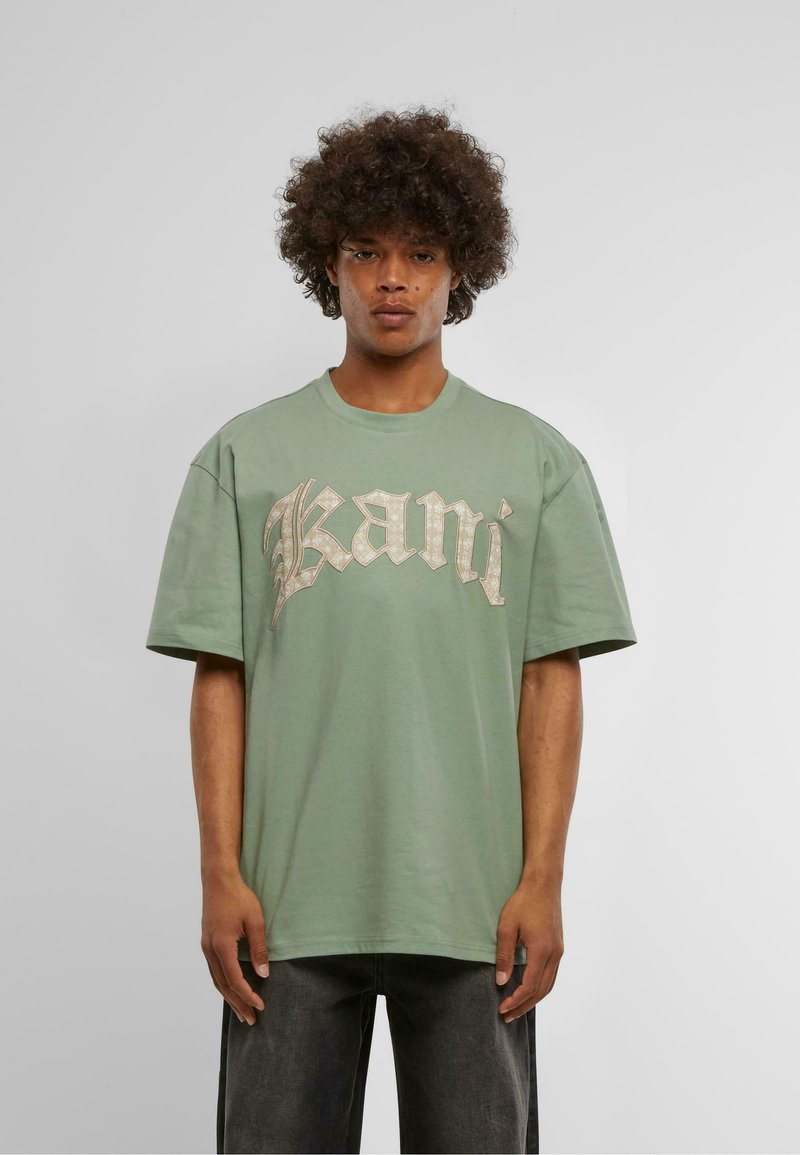 Light green cotton t-shirt with short sleeves. Features large scripted text "Kani" in a metallic gold accent across the chest.
