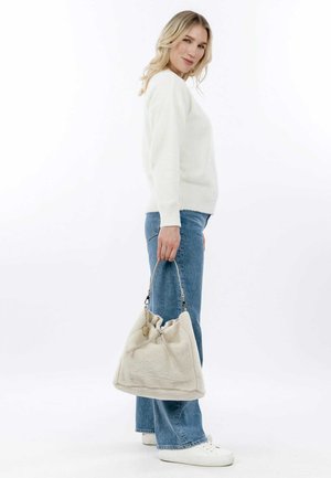 Beige, fluffy fabric handbag with a drawstring closure and short handle. Simple design, soft texture, and a small decorative metal accent.