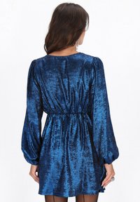 Sininen, kiiltävä minimekko, jossa on pitkät puffihihat, joustava vyötärönauha ja pehmeä tekstuuri. Takakuvassa näkyy sileä kangas.