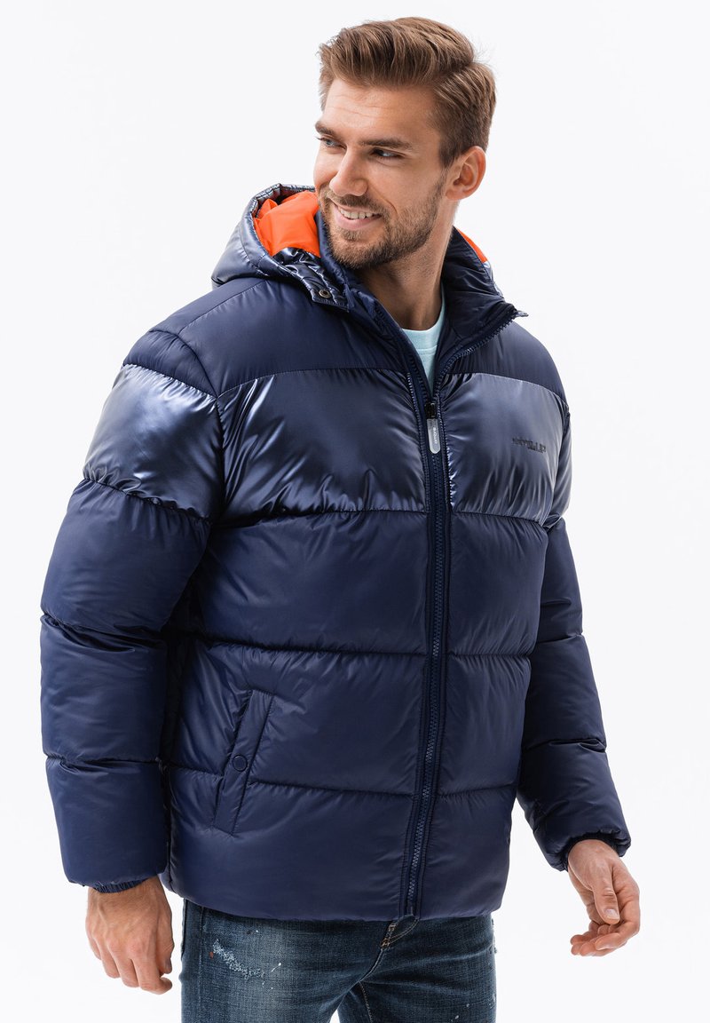 Marine pufferjack met een glanzende afwerking en een oranje voering van de capuchon. Voorzien van een ritssluiting aan de voorkant en twee zijzakken, ontworpen voor warmte en comfort.