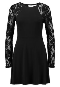 Czarna sukienka z długimi koronkowymi rękawami zdobionymi wzorami kwiatowymi. Góra jest dopasowana, przechodząc w rozkloszowaną spódnicę, co tworzy kobiecą sylwetkę.