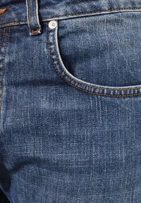 Jeans in denim blu scuro con un design classico, cuciture arancioni e dettagli con rivetti. Tessuto liscio con un leggero effetto sbiadito.