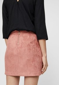 Mini falda de ante rosa con una cremallera visible en la parte posterior. Presenta una textura suave y un corte ajustado. Parte superior negra que cubre parcialmente la cinturilla.