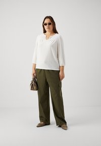 Baltas acs izgriezums blūze ar apkakles apaļu izgriezumu un trīs ceturtdaļu piedurknēm, apvienota ar olīvu zaļiem kravas biksēm. Aksesuāri ietver mazu brūnu somu.