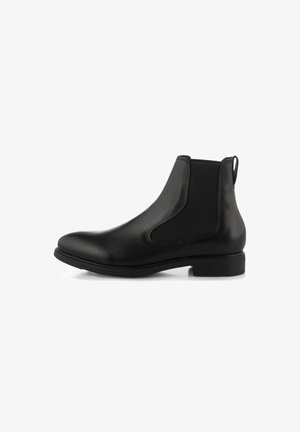 Botte Chelsea en cuir noir avec panneaux latéraux élastiques, talon bas, bout rond et languette à l’arrière sur fond blanc.