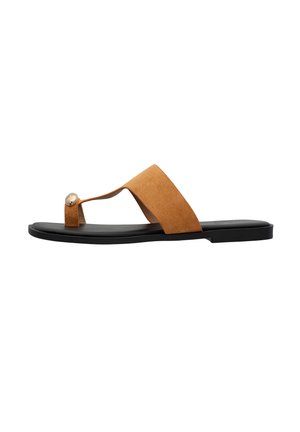 Beige Wildleder Flip-Flop Sandale mit einem Kreuzband-Design, dekorativem runden Niete und einer flachen schwarzen Gummisohle. Glatte Textur mit minimalen Akzenten.