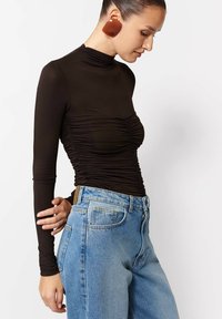 Czarna bluzka z długim rękawem i marszczeniami, dopasowany krój, w zestawie z jasnoniebieskimi jeansami wysokimi w talii z kieszeniami i zapięciem na zamek.