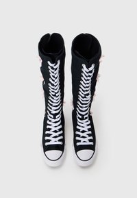 Mustad mustat kangastossud valgete silmadega ja ülekaaluliste paeltega. Omab roosade aktsentidega külgedel, ümmargust varbaosa ja valget kummist tallat.