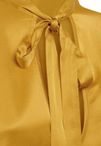 Blusa di raso gialla con neck tie, caratterizzata da una texture liscia, un profondo scollo e un dettaglio a fiocco annodato al colletto.