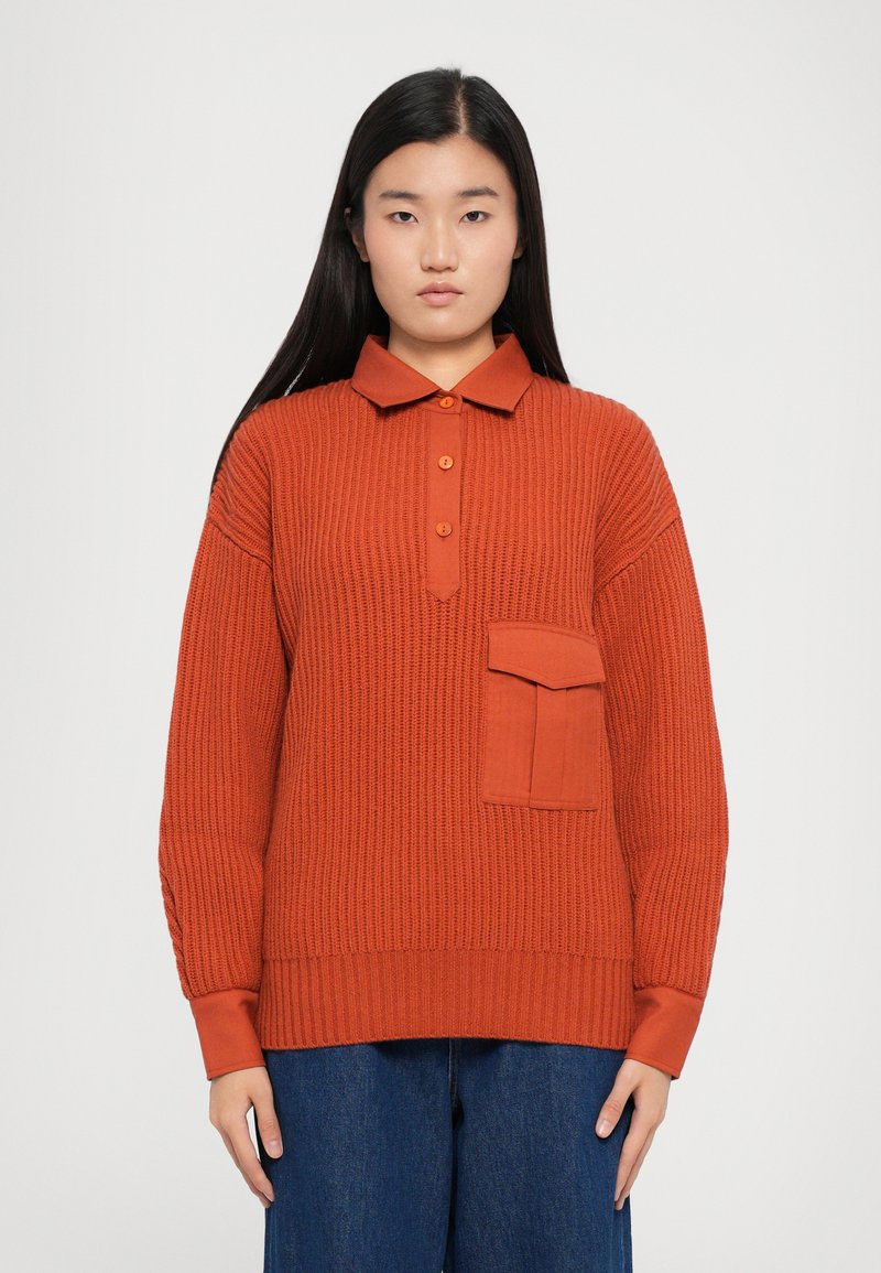 Geribbelde, verbrande oranje pullover met een kraag, knoopsluiting aan de voorkant en een enkele borstzak. Bevat lange mouwen met contrasterende manchetten.