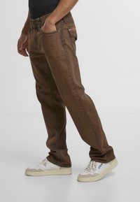 Pantalones de mezclilla marrones de corte recto, con detalles de costura y bolsillos laterales, combinados con zapatillas blancas.
