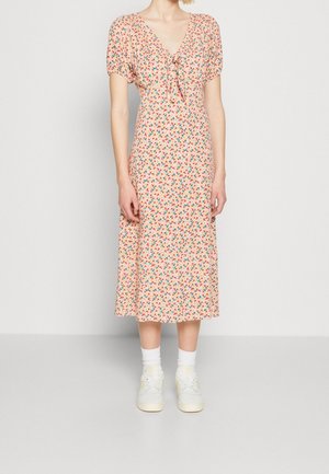 Femme portant une robe midi pêche avec des manches ballon et un petit imprimé floral multicolore, associée à des chaussettes blanches et des baskets.